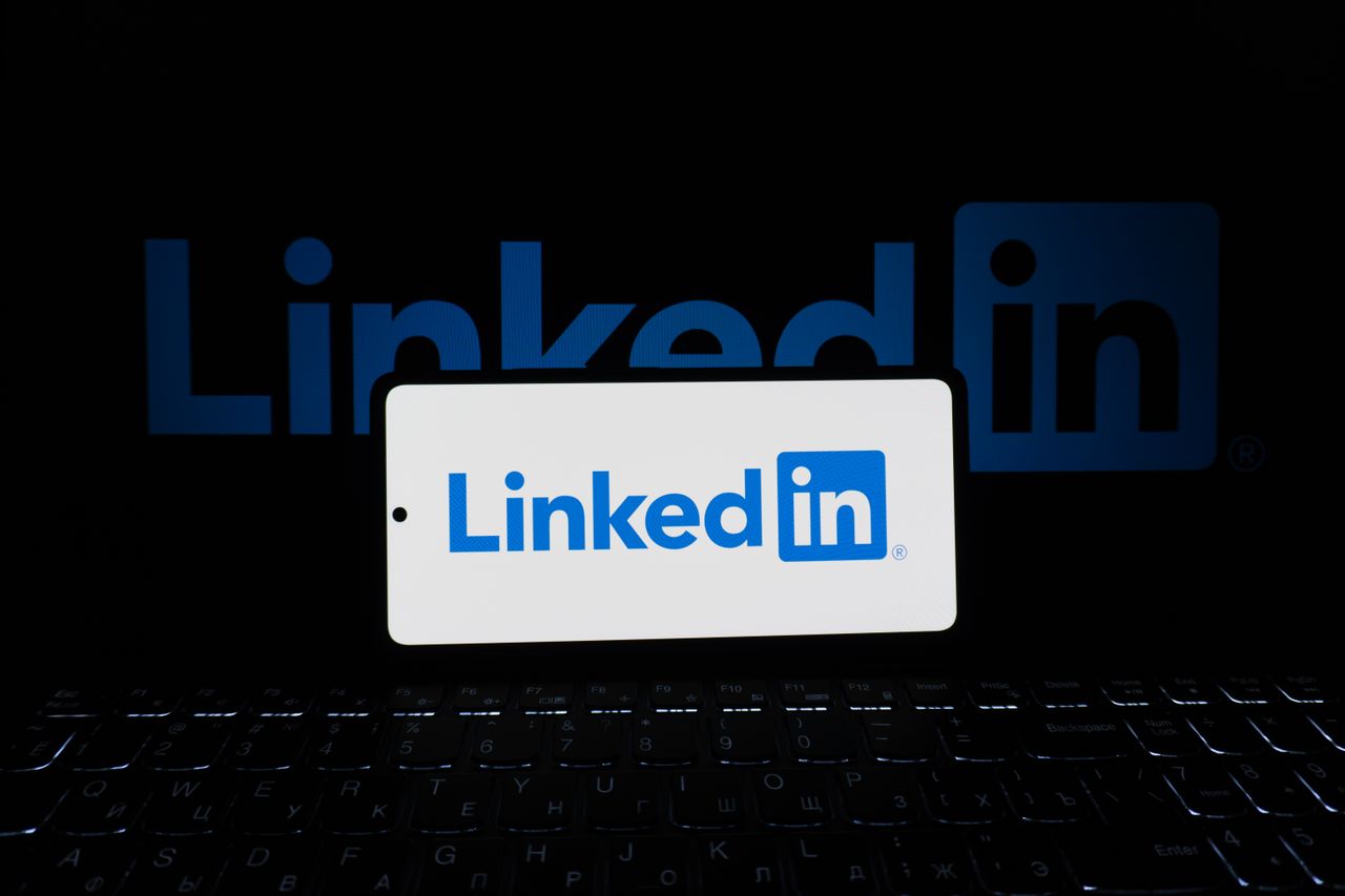 Smartphone montrant le logo LinkedIn avec clavier et grand logo en arrière-plan, thème professionnel.